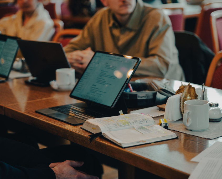 Student in dining room of the European Theological Seminary having an open bible and learning on an iPad.