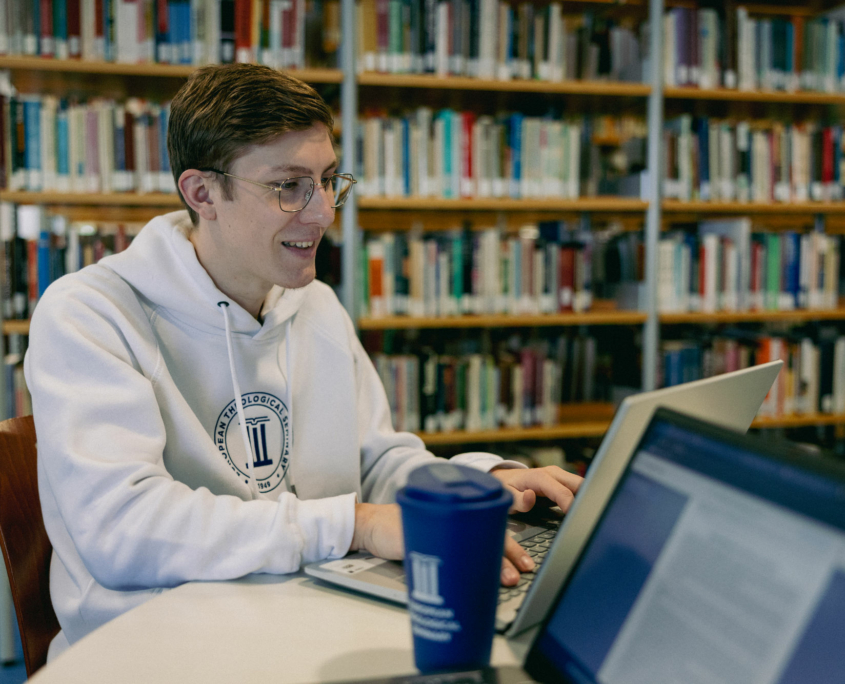 A student of the European Theological Seminary is learning and smiling while doing so in the library